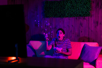 Young man enjoying leisure time indoors, watching television with popcorn during a vibrant evening,...