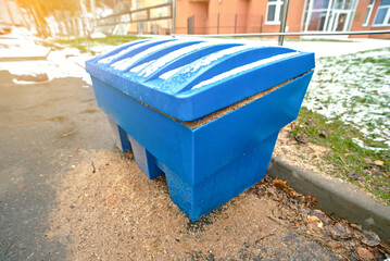 Fototapeta premium Blue storage grit bin placed for winter sand treatment to reduce slippery sidewalks and icy road hazards, ensuring public safety during cold weather. Grit bin covered with snow