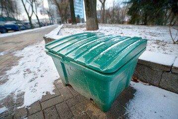 Green grit bin filled with sand placed on sidewalk for traction treatment and winter road safety,...