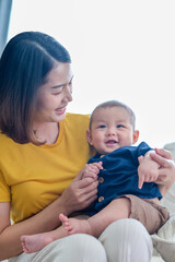Asian woman with her son holding him by her hand. Happy baby boy was holding by his mother. Asian family with little boy at home enjoy tender family moment, motherhood.