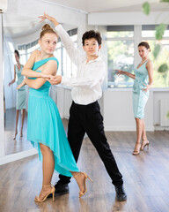 Experienced female dancer teaches tango to pair of teenagers in the ballroom