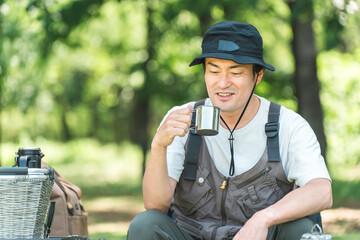 キャンプ場でキャンプ・グランピングを楽しむ男性（水・コーヒー・ビールをを飲む）
