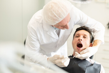 Man is sitting in armchair during dental diagnosis at dentist appointment. Senior man doctor...