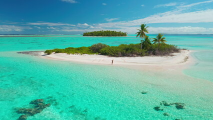 Aerial view of a woman raising her arms on a pristine white sand beach of a tropical island surrounded by turquoise water