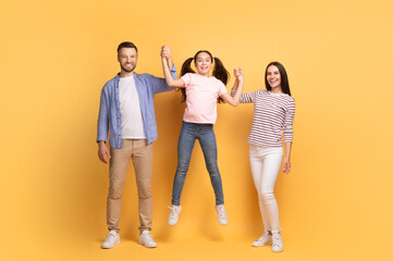 A loving family shares a joyful moment as the mother and father lift their smiling teenage daughter off the ground.