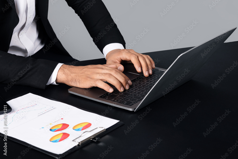 Poster Unrecognizable man in business attire is focused on his laptop, analyzing data. Nearby, a document with colorful pie charts is neatly arranged on the table.