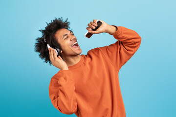 A young African American man expresses joy while listening to music through headphones. He sings along passionately, showcasing a vibrant lifestyle against a blue background.