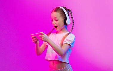 A cheerful girl with braided hair plays a mobile game while wearing stylish headphones. Vibrant...