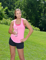 Beautiful young Caucasian woman in workout gear pauses from outdoor work-out with bottle of water