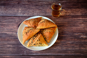 A plate with several fresh meat pies decorated with caraway seeds and a cup of hot tea on a wooden table.