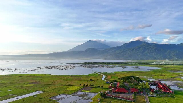 Drone view of amazing tropical lake with mountain background. Green agricultural plantation on the lake side. Aerial scenery of Rawa Pening Lake, Indonesia.