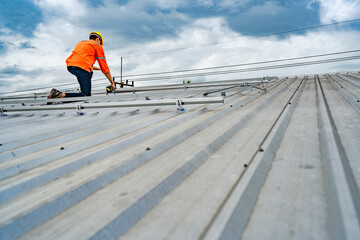 Technician in safety uniform and helmet kneeling on a rooftop, using a drill for precise...