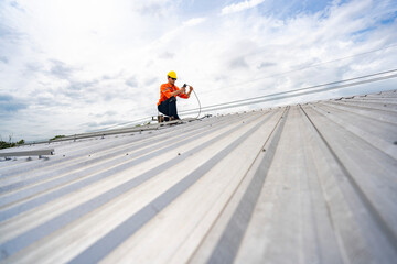 Technician in safety uniform and helmet kneeling on a rooftop, using a drill for precise...