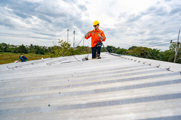 Technician in safety uniform and helmet kneeling on a rooftop, using a drill for precise installation work. A scene highlighting safety, professionalism, and technical expertise in construction.