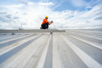 Technician in safety uniform and helmet kneeling on a rooftop, using a drill for precise...