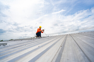 Technician in safety uniform and helmet kneeling on a rooftop, using a drill for precise...