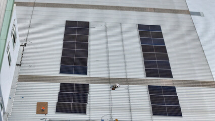 technician in safety gear inspects solar panels on a metal rooftop, holding a tool. The scene emphasizes renewable energy, solar technology, and maintenance of sustainable infrastructure.