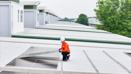 technician in hard hat and safety gear inspects solar panels on a metal rooftop, holding a tool....