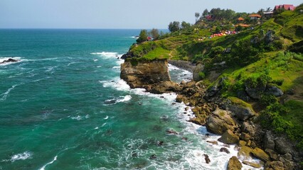 Aerial drone view of coastline with hills and trees, as well as view of coral cliffs and sea with waves from the ocean in Menganti Beach Kebumen Central Java Indonesia