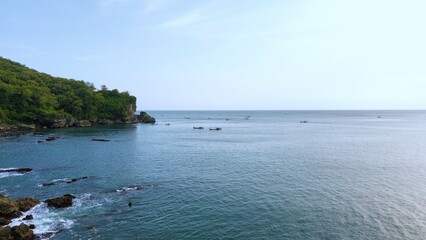Aerial drone view of coastline with hills and trees, as well as view of coral cliffs and sea with waves from the sea in Pedalen Beach Kebumen Central Java Indonesia