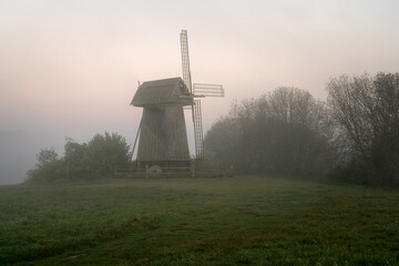 View of an ancient wooden windmill on the banks of the Sorot River on a foggy summer morning, Mikhailovskoye, Pushkinskiye Gory, Pskov region, Russia