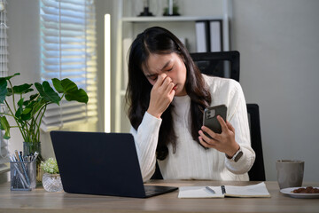 Young asian businesswoman rubbing her eyes, suffering from eye strain after working on laptop...