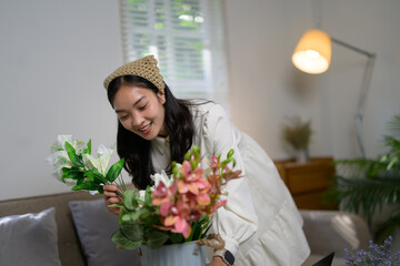 Smiling young asian florist arranging a vibrant bouquet of colorful flowers in a stylish metal vase, crafting an eye-catching centerpiece perfect for enhancing home decor and interior design