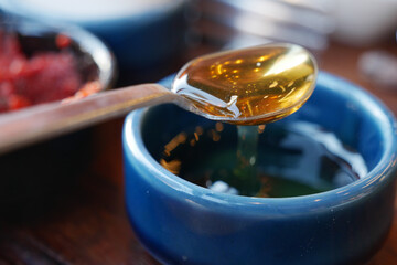 Golden Honey is Dripping Lavishly from the Spoon into the Blue Bowl