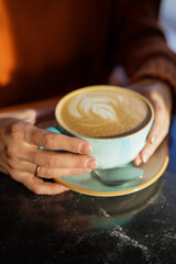 A cup of coffee held in hands. Foamy decorated cappuccino