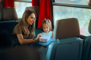 Mother and Daughter Opening a Lunchbox in a Train. Family having a snack while using public transportation for vacationing 
