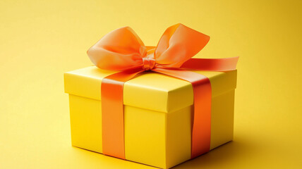 Obraz premium Pretty gift box with yellow wrapping and orange ribbon on a yellow studio background and space for text