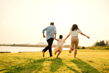 Asian family having fun and enjoying the nature, holding hands running and playing together in a green garden on a sunny day, happy family day