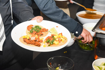 A person is holding a plate with three tacos on it
