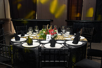 A black and gold table setting with a tablecloth and black chairs
