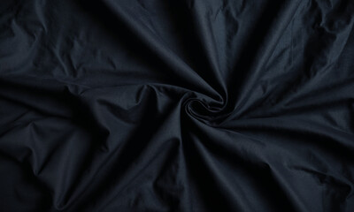 A close-up of black fabric featuring smooth folds and a spiral swirl pattern, creating an elegant and dramatic texture that highlights the simplicity and beauty of dark textiles.