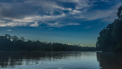 Early morning in a tropical rain forest. The bed of a calm river, ripples, reflection on the surface of the water. Thickets of trees on the banks.  Blue sky, clouds. Malaysia.Borneo.Kinabatangan River