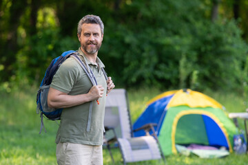 Naklejka premium Man on camp in the forest with tent. Man hiker outdoor on a summer day. Summer camp and nature vacation. Man on summer camping. Camp adventure. Hiking concept. Camping tent. Copy space