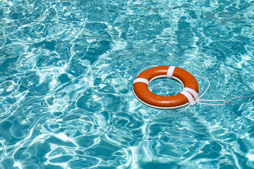 Drowning concept. No swimming. Rescue swimming ring in water. Safety water equipment. Lifebelt on sea or pool. Orange inflatable ring floating in blue water. Rescue at pool.