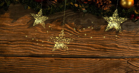 Fototapeta premium Image of gold christmas stars swinging from tree over wood
