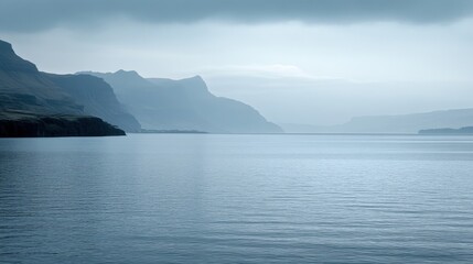 Tranquil Blue Landscape with Misty Mountains and Calm Water Reflections