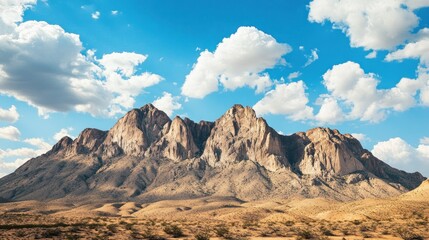 Naklejka premium Majestic mountain range under a vibrant blue sky with fluffy clouds.