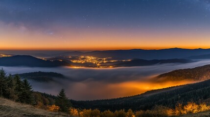 Obraz premium Serene Sunset Over Mountains and Foggy Valley with Illuminated Town Below