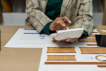 A person is using a calculator to add up numbers on a piece of paper. The paper has a budget and a graph on it