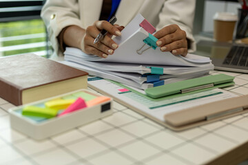 A woman is holding a stack of papers on a desk. The papers are organized and labeled with different...