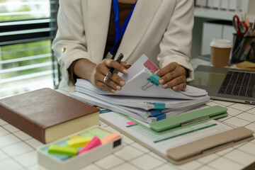 A woman is holding a stack of papers on a desk. The papers are organized and labeled with different...