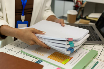 A woman is holding a stack of papers on a desk. The papers are organized and labeled with different...
