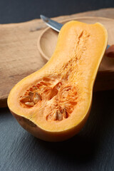 butternut squash cut in half revealing vibrant orange flesh and seeds on cutting board with knife and wooden bowl in background, soft focus with copy space