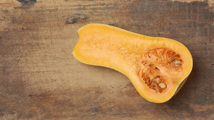 butternut squash cut in half revealing vibrant orange flesh and seeds on cutting board background,...