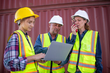 Engineer or dockworker working in the construction container dock yard checking and inspection containers data on computer program environment is container shipping Logistics business concept.