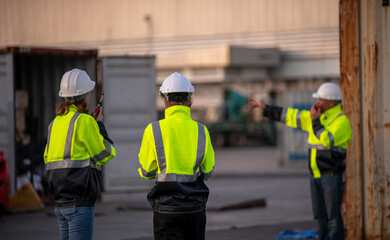 Engineer or dockworker working in the construction container dock yard checking and inspection containers data on computer program environment is container shipping Logistics business concept.